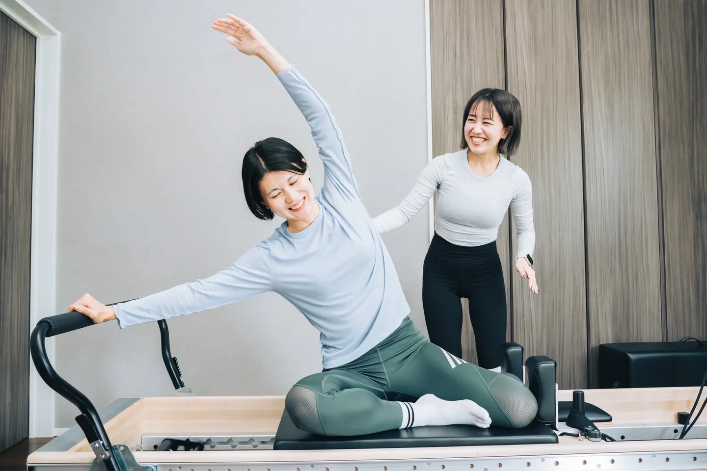 リフォーマーの上で体を横に倒している受講者に、Yukaさんが横で声をかけている様子