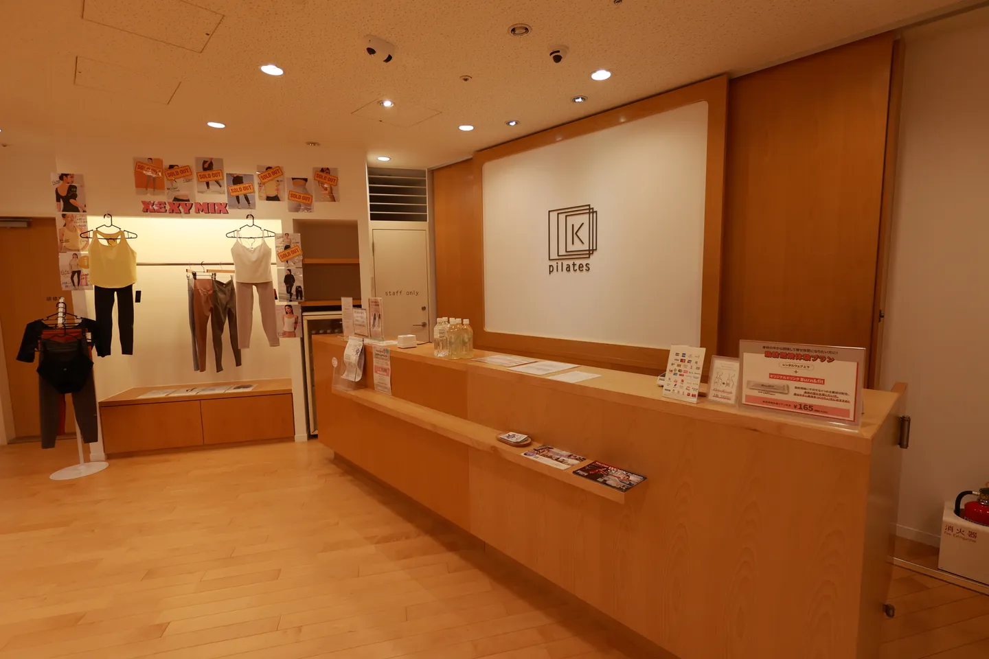 木目の受付カウンターと、左手にウェアが掛けられた物販コーナー