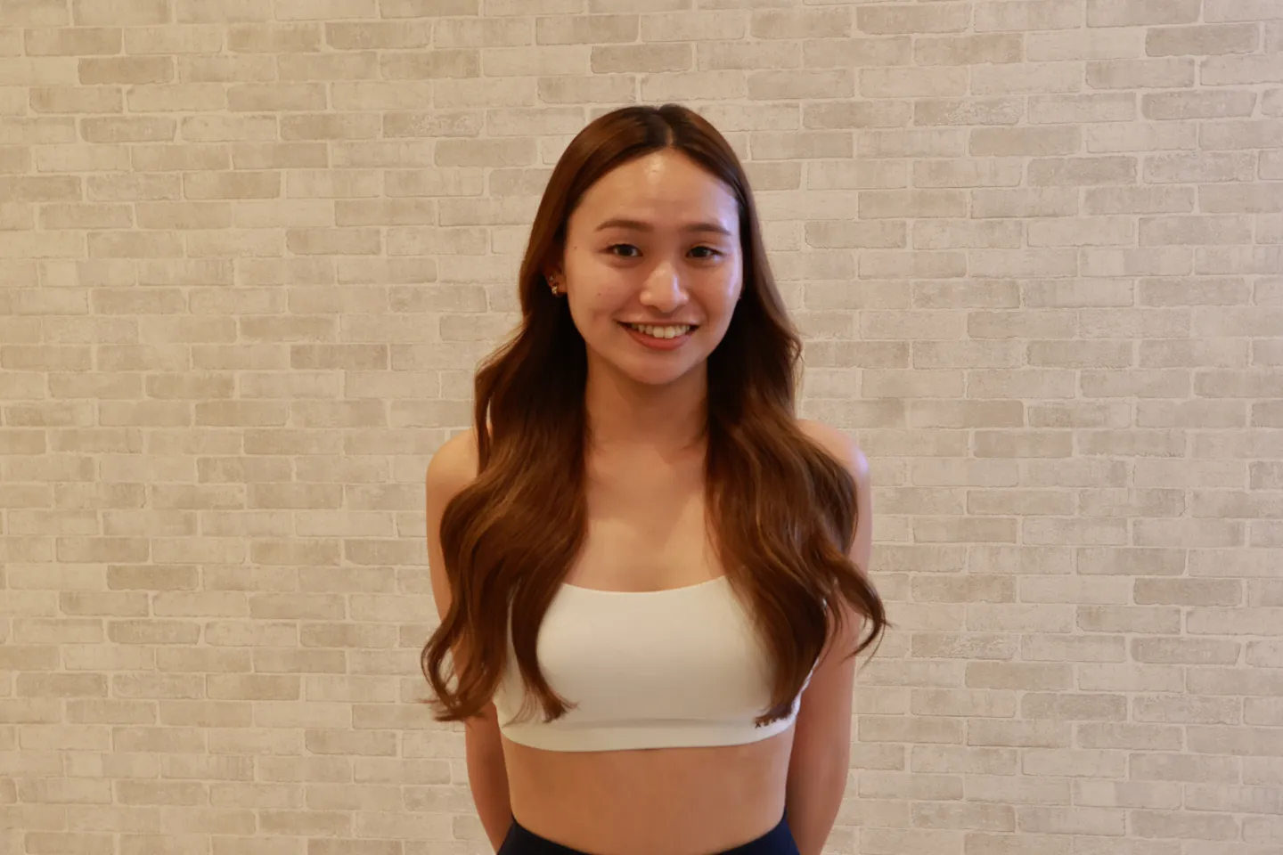 スタジオの壁の前に立つ、pilates K 中目黒店のインストラクター maikaさん