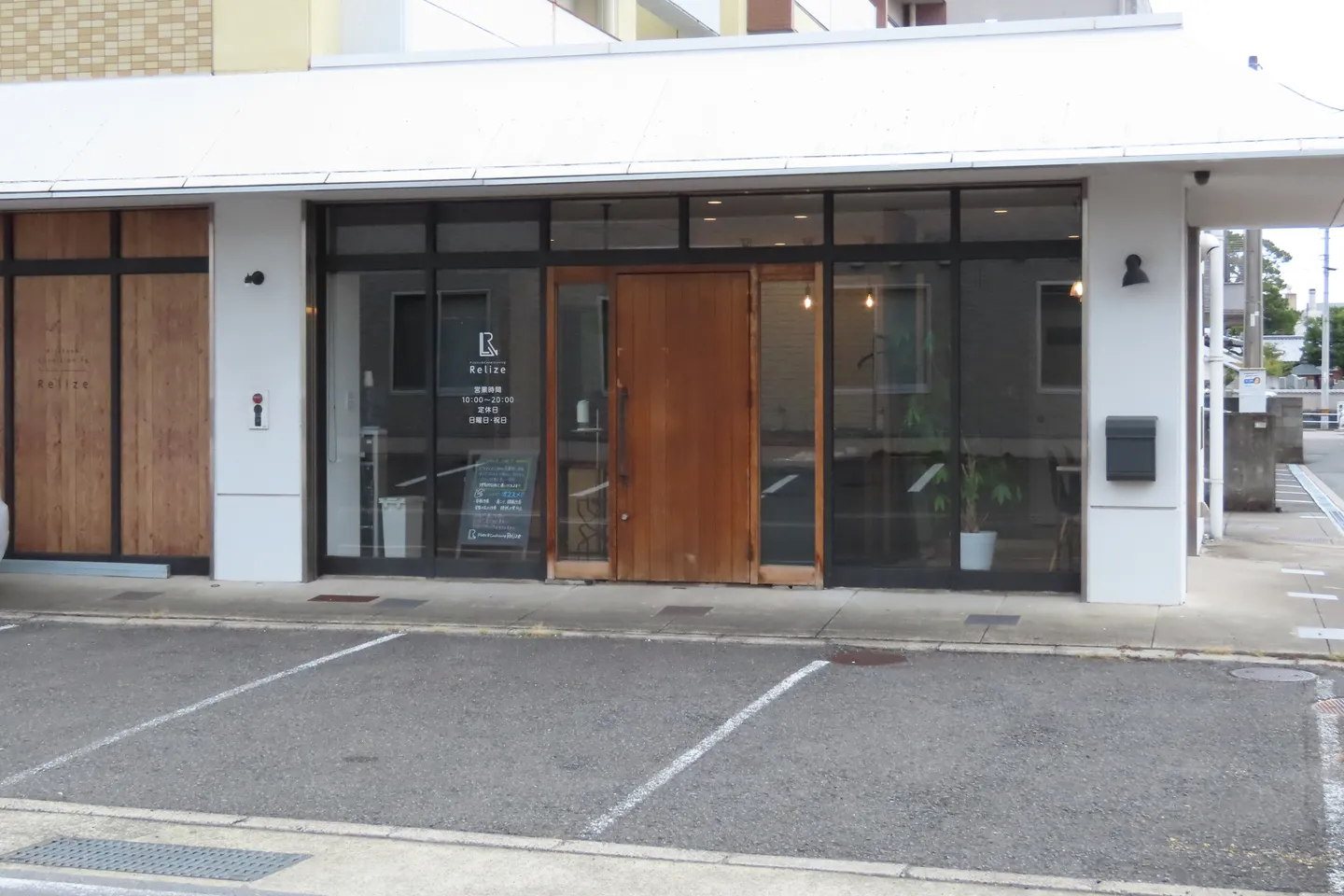 Relize 福島店の外観。ガラス張りの店先の中央に木の扉があり、店の前に白線で区切った駐車区画が並んでいる