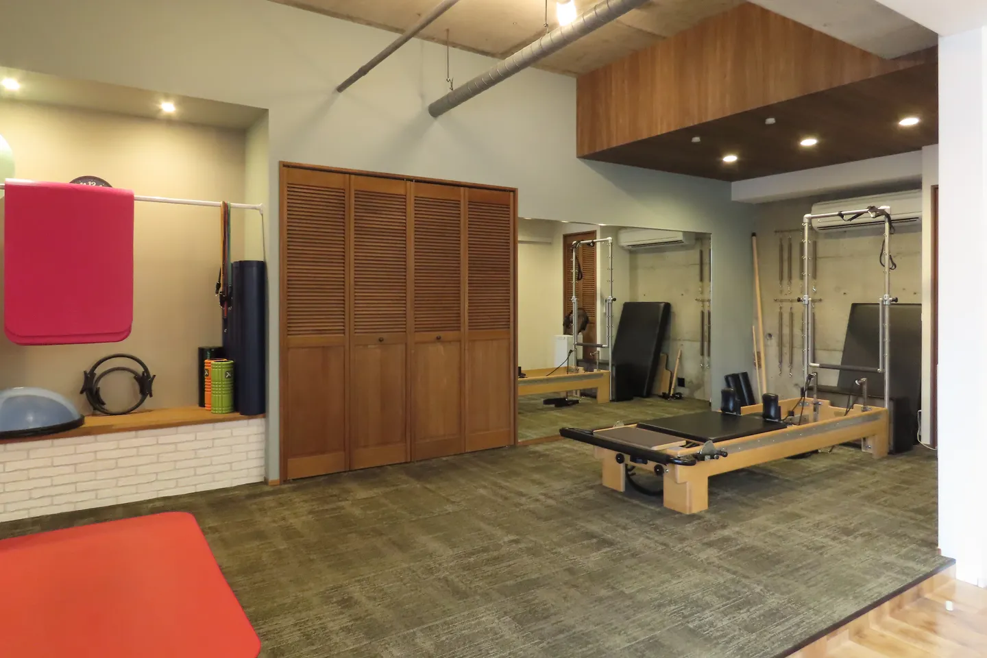 Relize 福島店のスタジオ。タワー付きのリフォーマーと鏡があり、左手の棚にマットやストレッチポールなどの小道具が置かれている