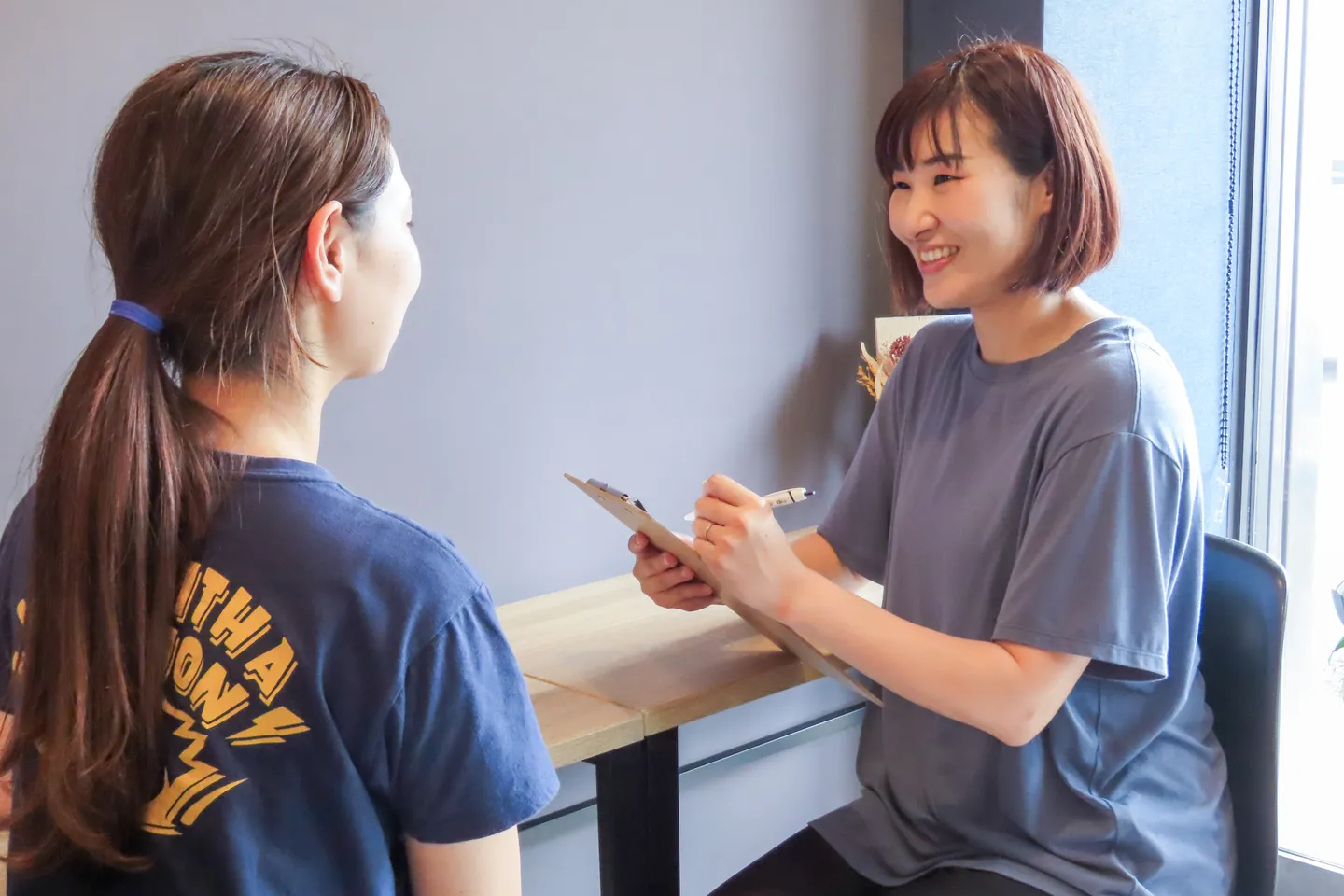 クリップボードを手に、向かいに座った方の話を聞きながら記録するスタッフ